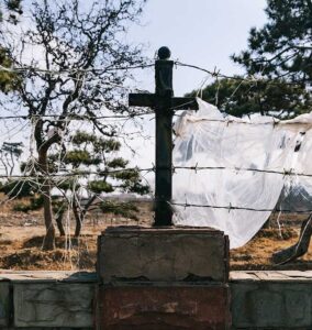 black cross on brown brick wall strung with barbed wire